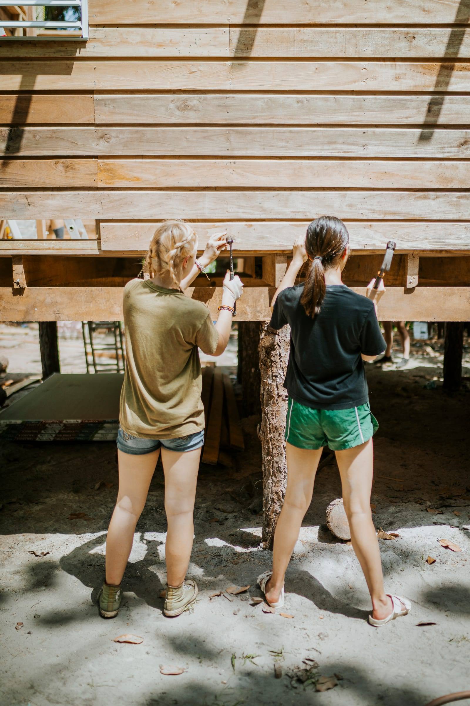 Two volunteers hammer boards beneath a home raised on stilts