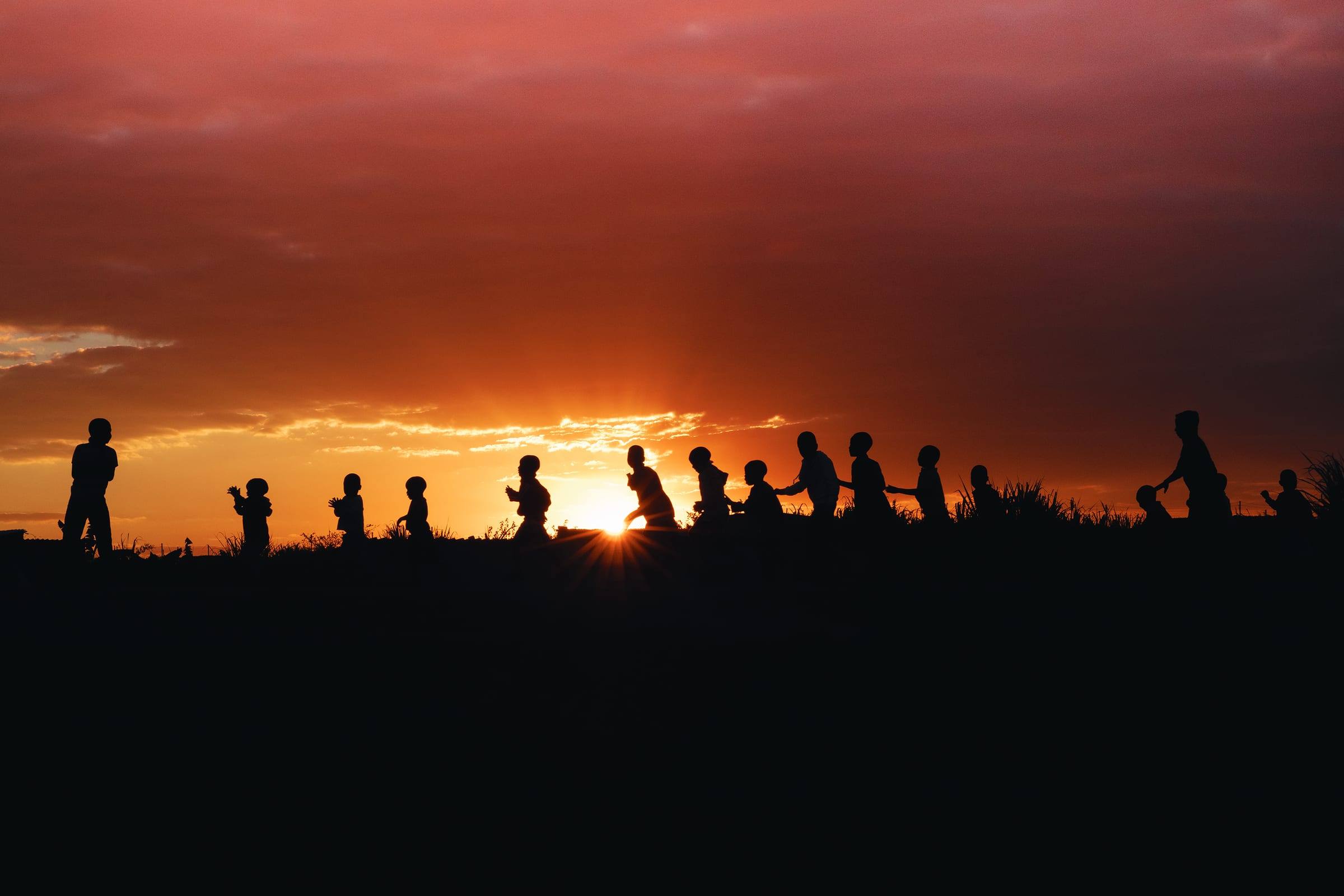 Children walk in a line across a field at sunset